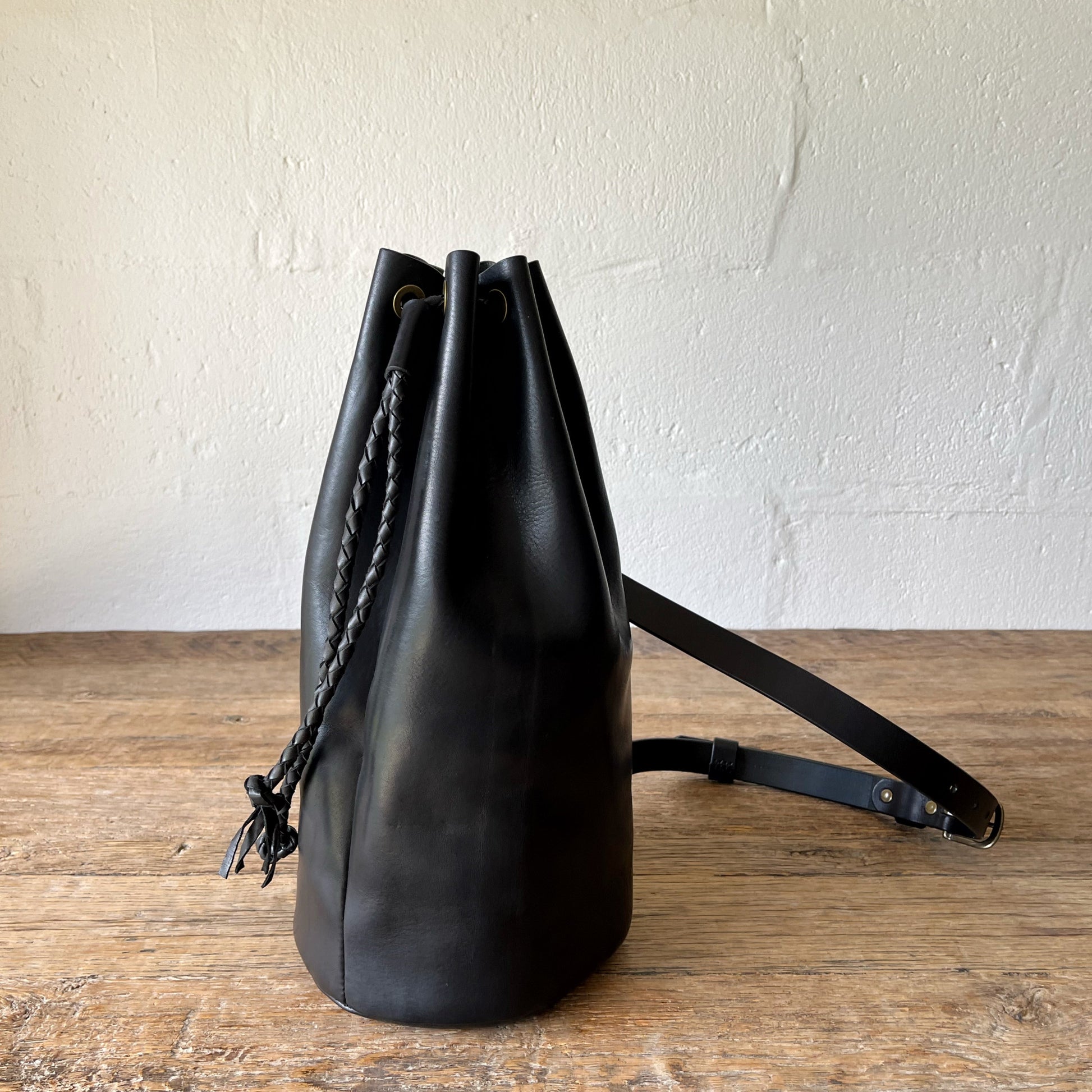Black leather backpack on a wooden surface with a white wall background