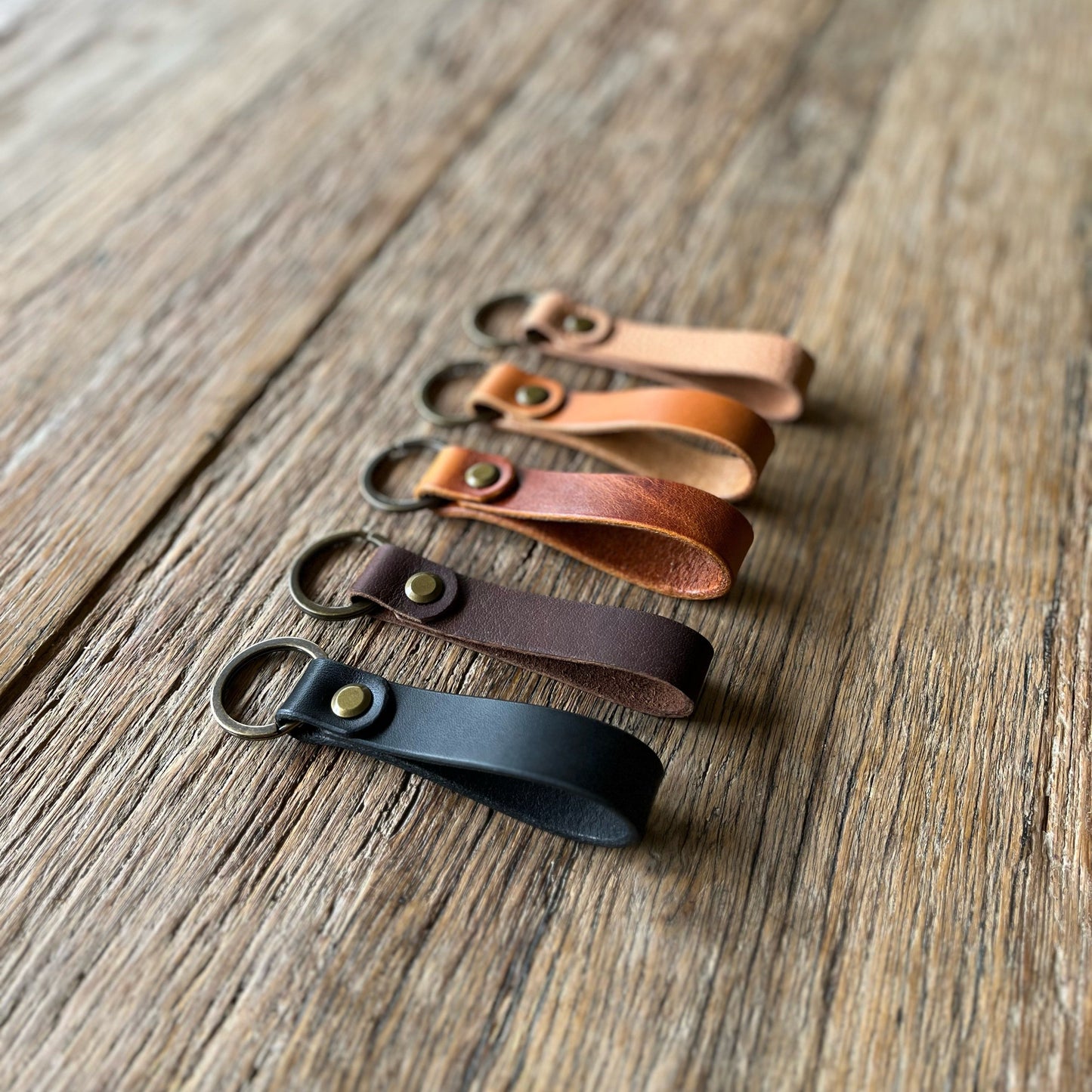 A collection of leather loop keyfobs in various colors displayed on a wooden surface.