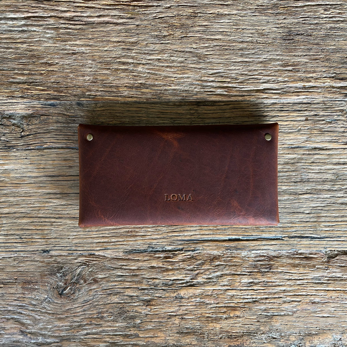 A dark brown leather wallet with the brand name 'LOMA' embossed on the front, displayed flat on a rustic wooden surface.