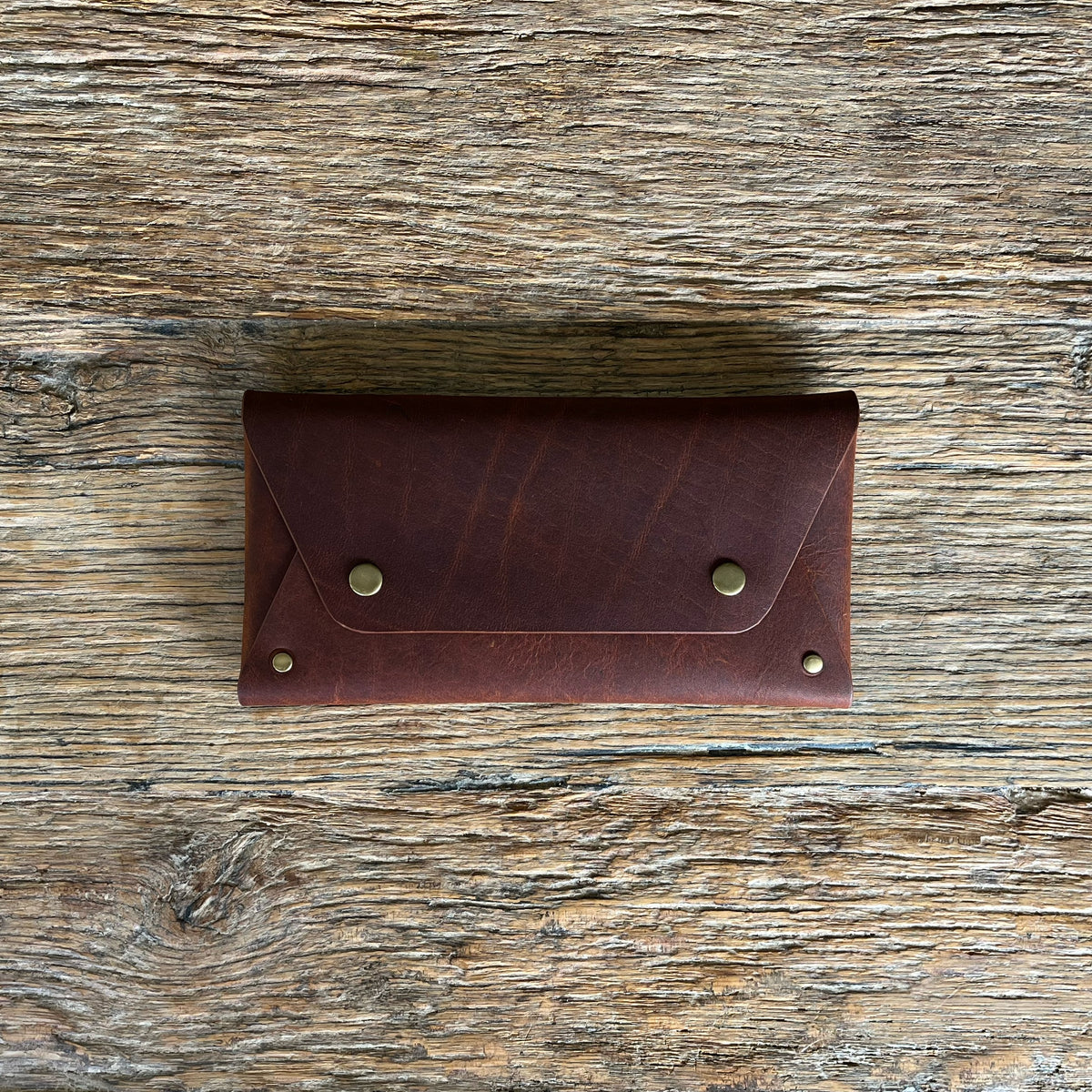 A dark brown leather wallet with brass snap buttons, laid flat on a rustic wooden surface.