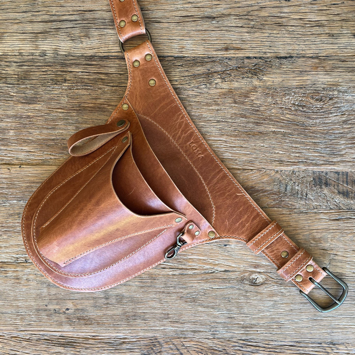 Brown leather tool belt with metal buckle on a wooden surface