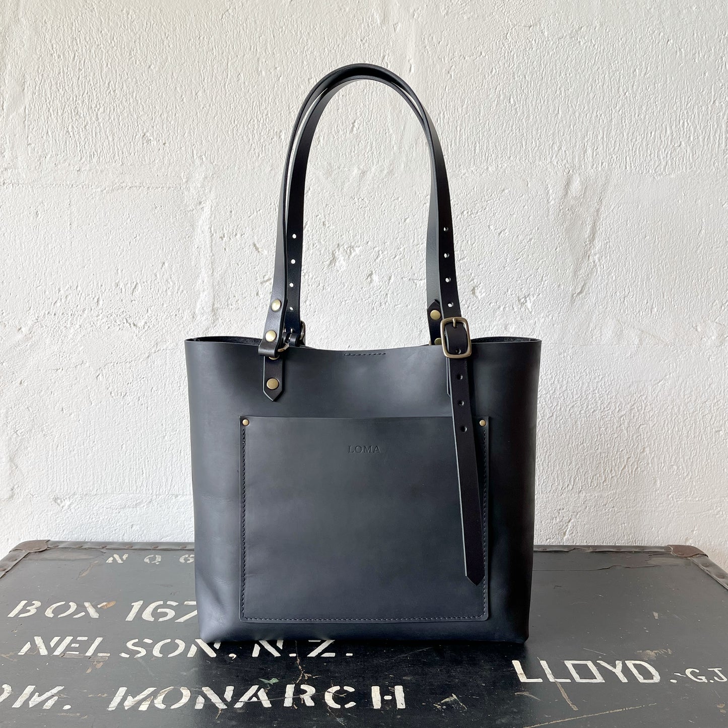 Black leather tote bag on a textured surface with a white wall background