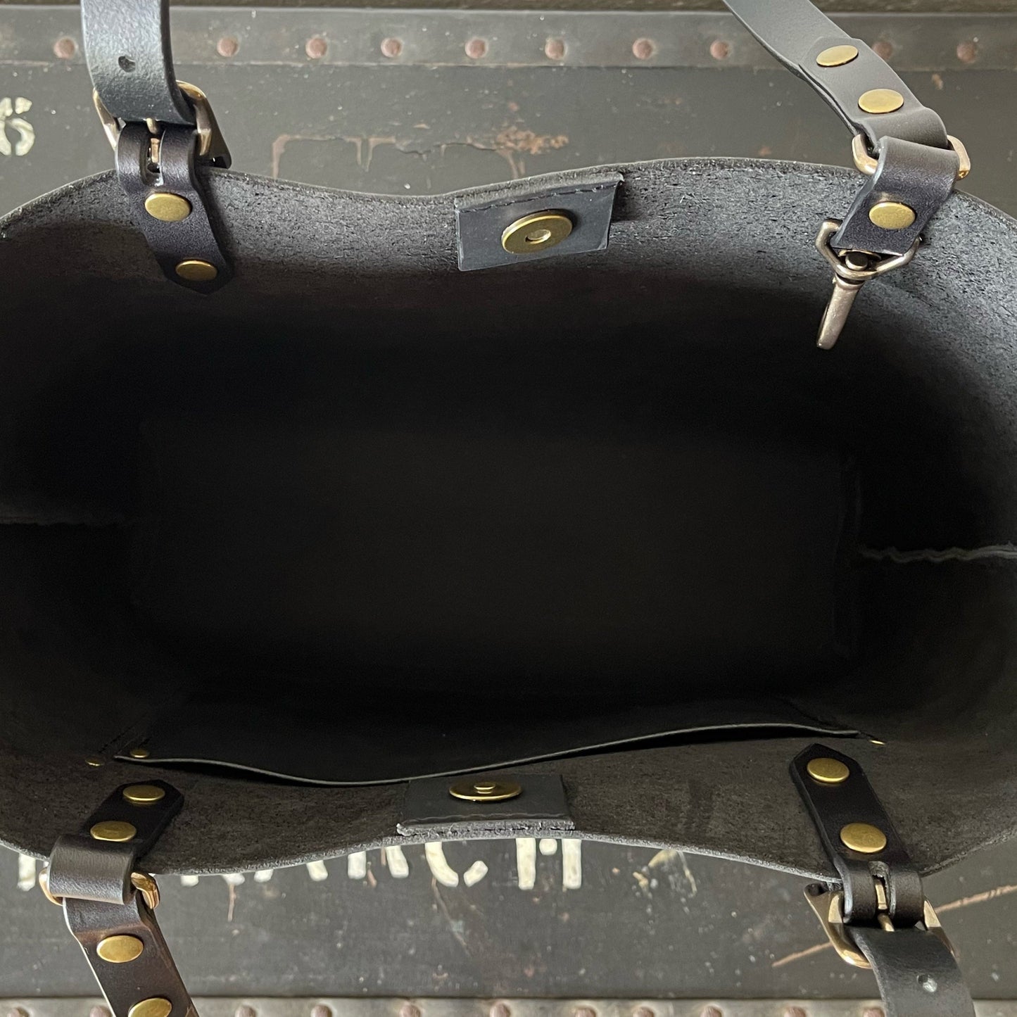 Close-up of a black leather bag with brass rivets on a dark background
