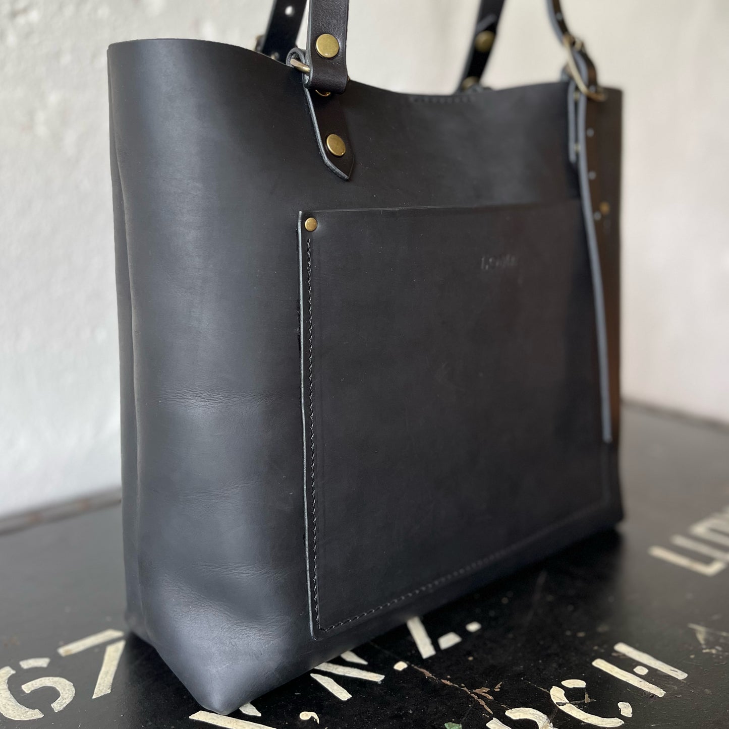 Black leather tote bag with brass hardware on a textured surface