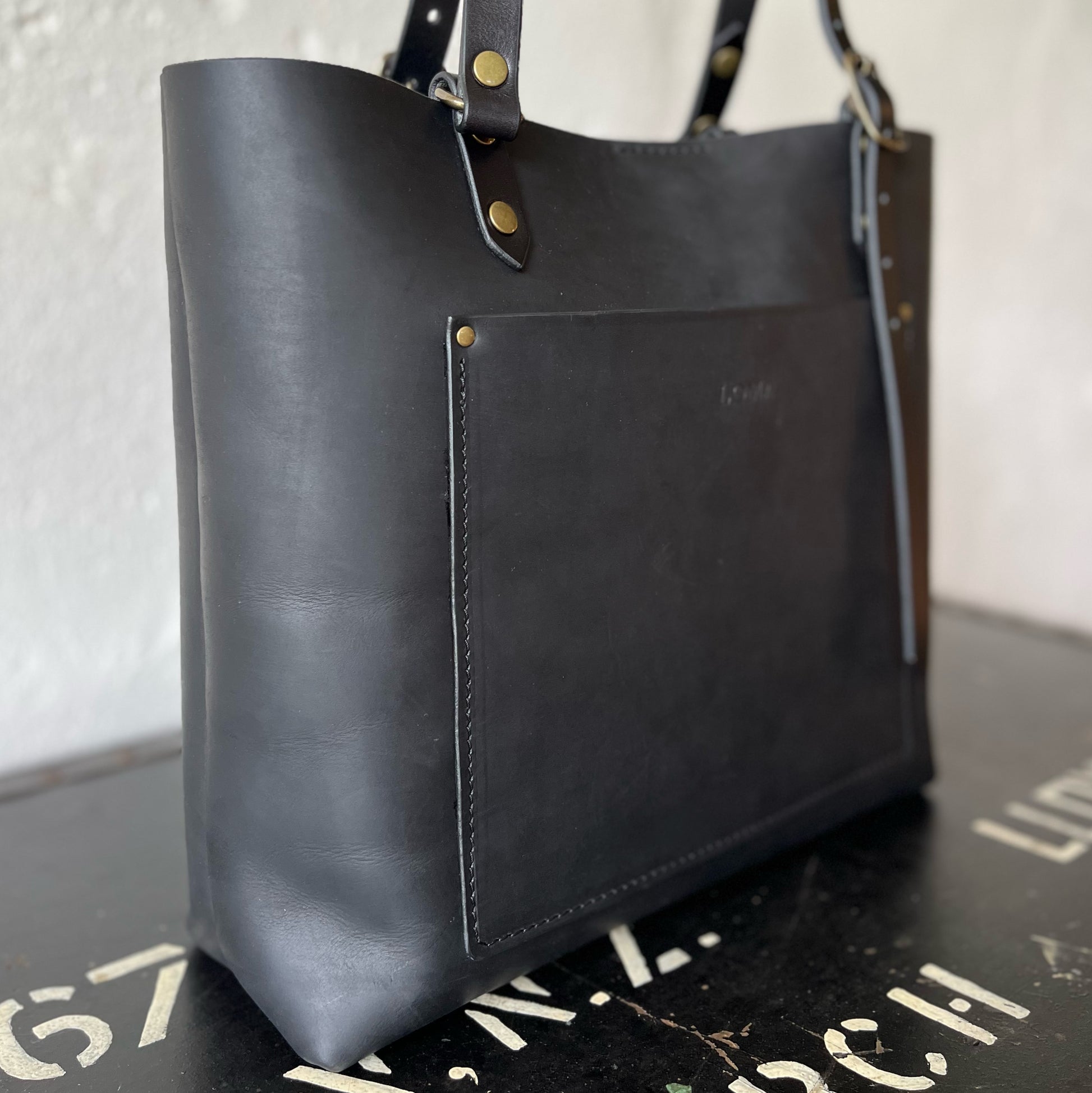 Black leather tote bag with brass hardware on a textured surface