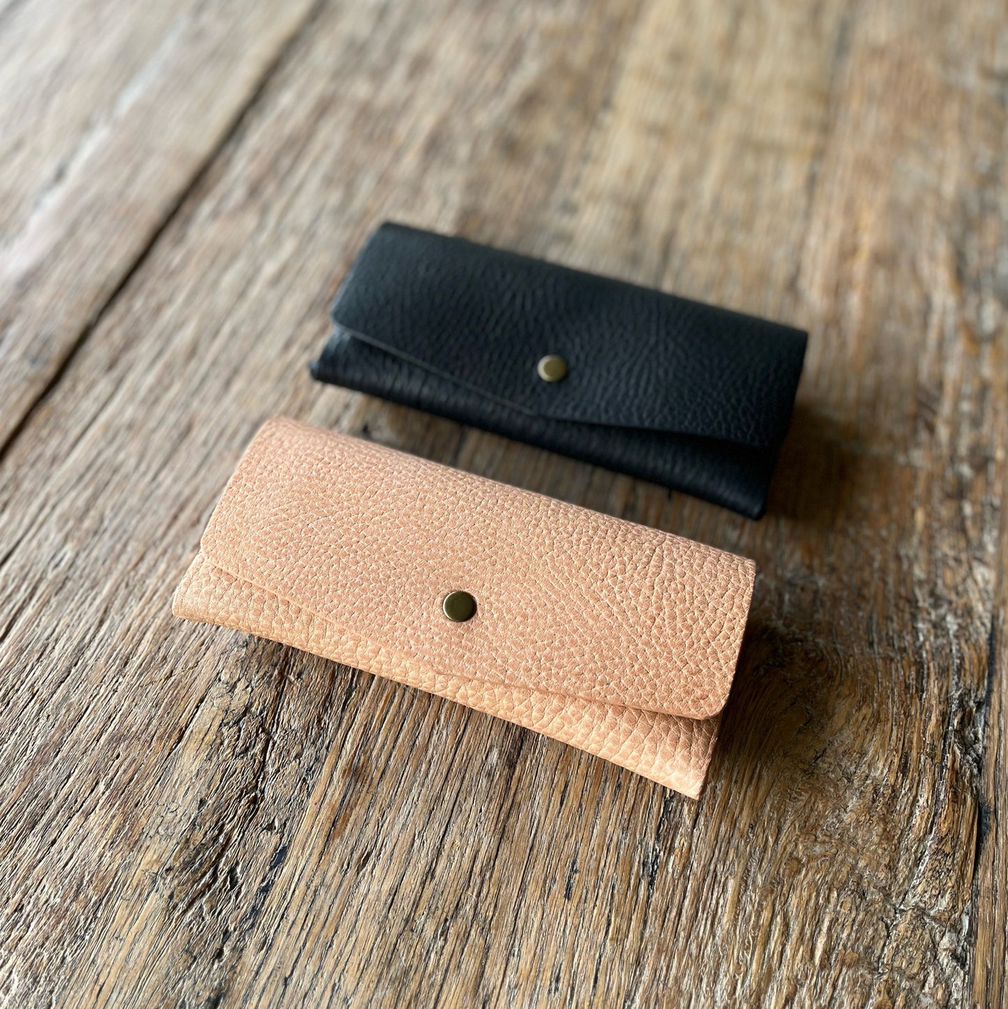 Two leather glasses cases one black and one natural, on a wooden surface.