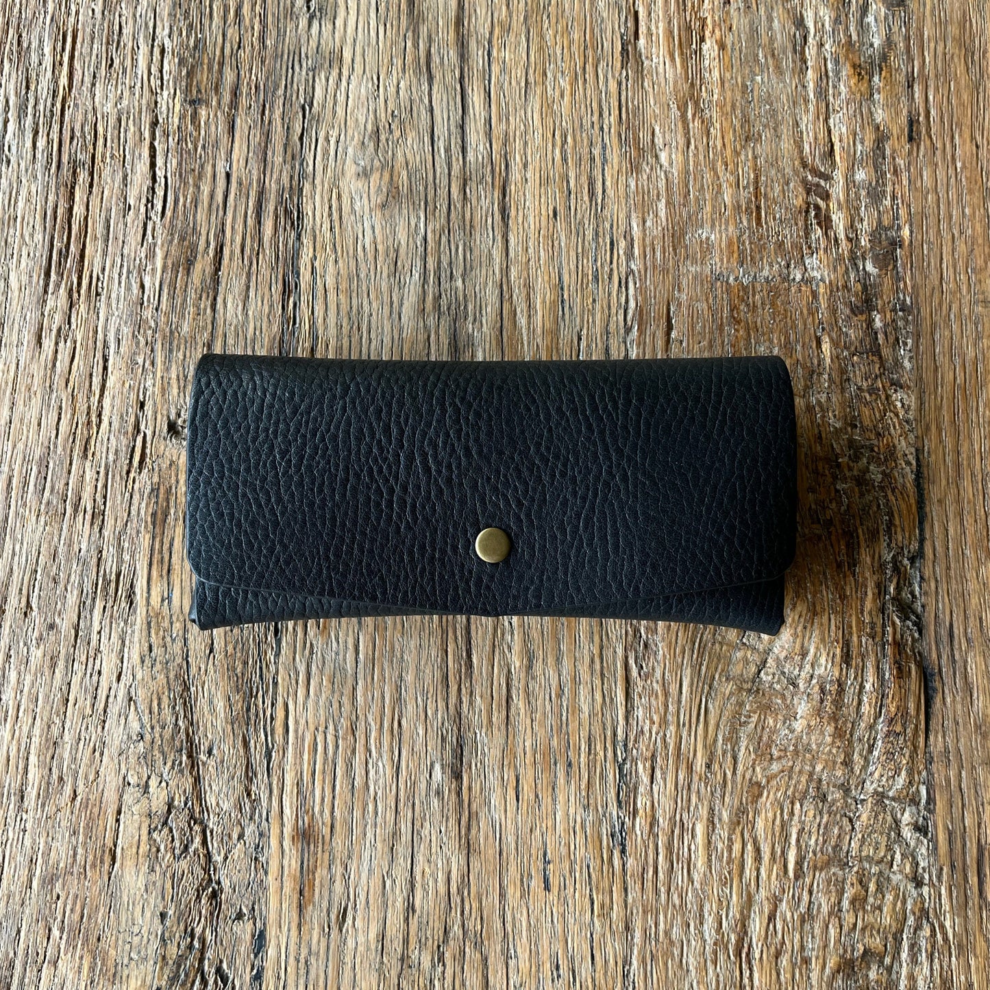 Black leather glasses case with a brass button on a wooden surface