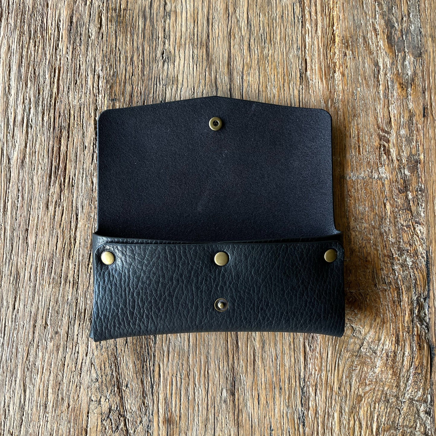 Black leather glasses case, open with brass rivets on a wooden surface