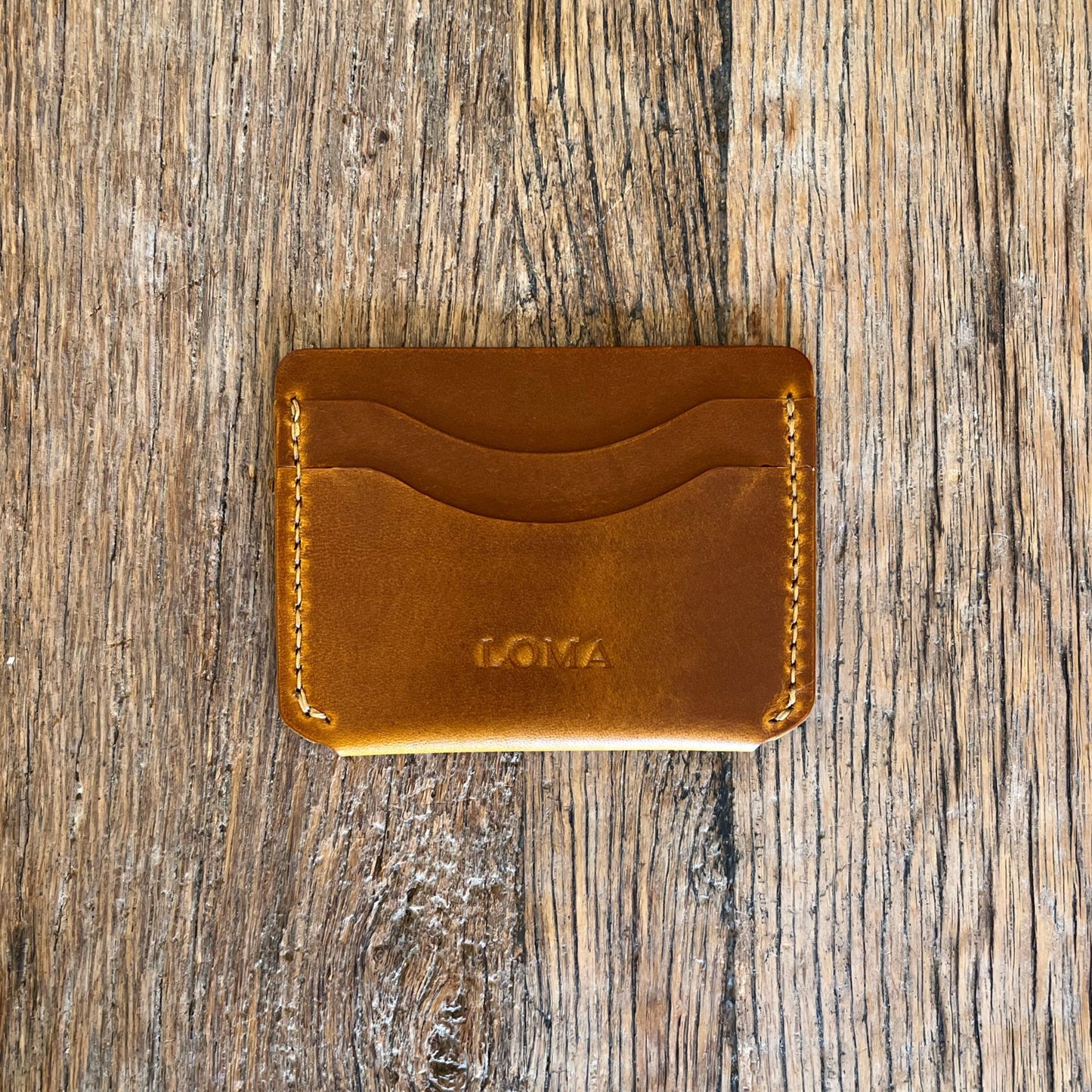 Brown leather cardholder with 'LOMA' branding on a wooden surface