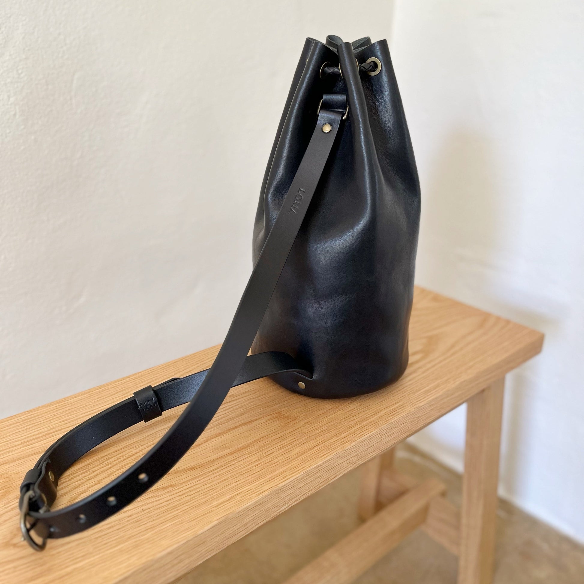Black leather bag with strap on a wooden surface against a white wall
