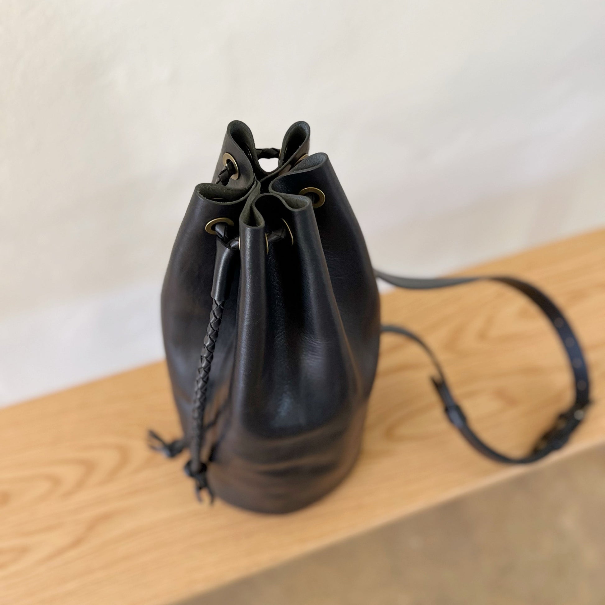 Black leather drawstring bag on a wooden surface with a white background