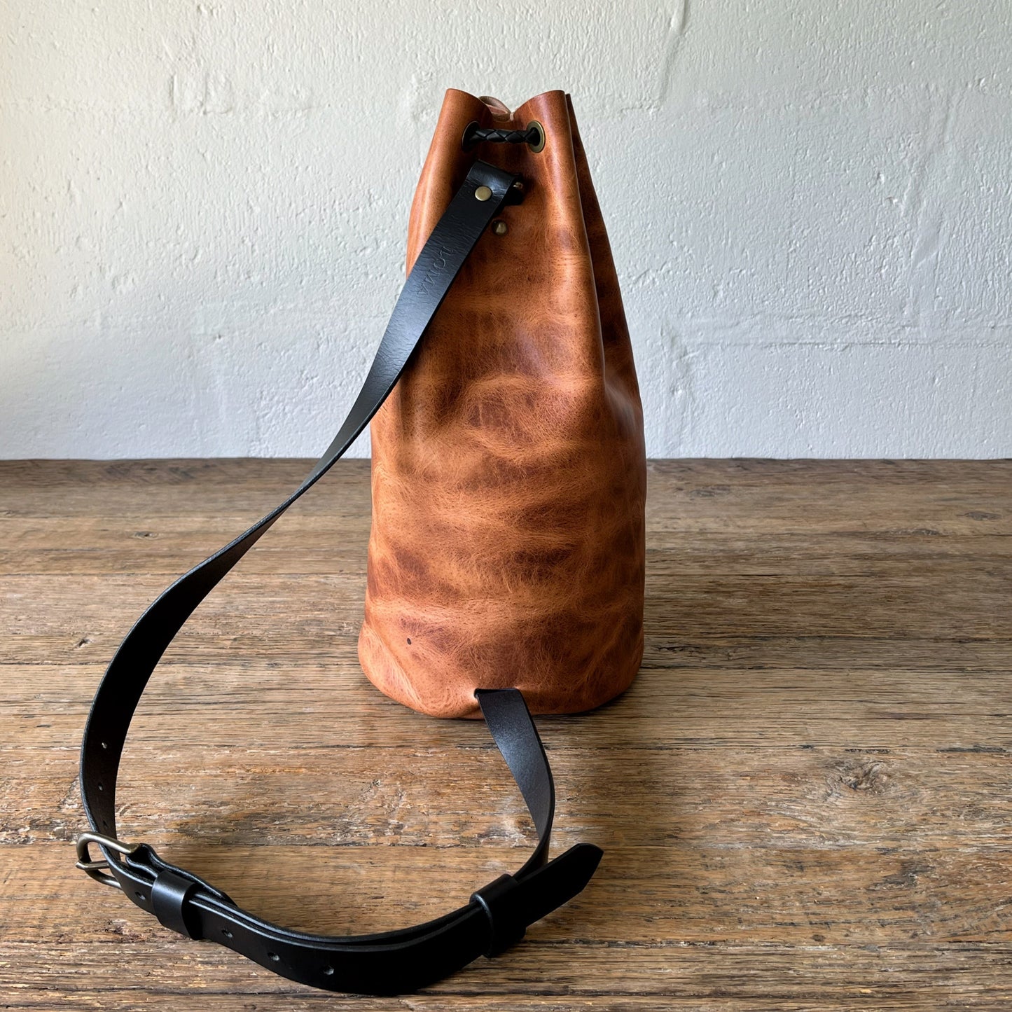 Brown leather bag with black strap on a wooden surface