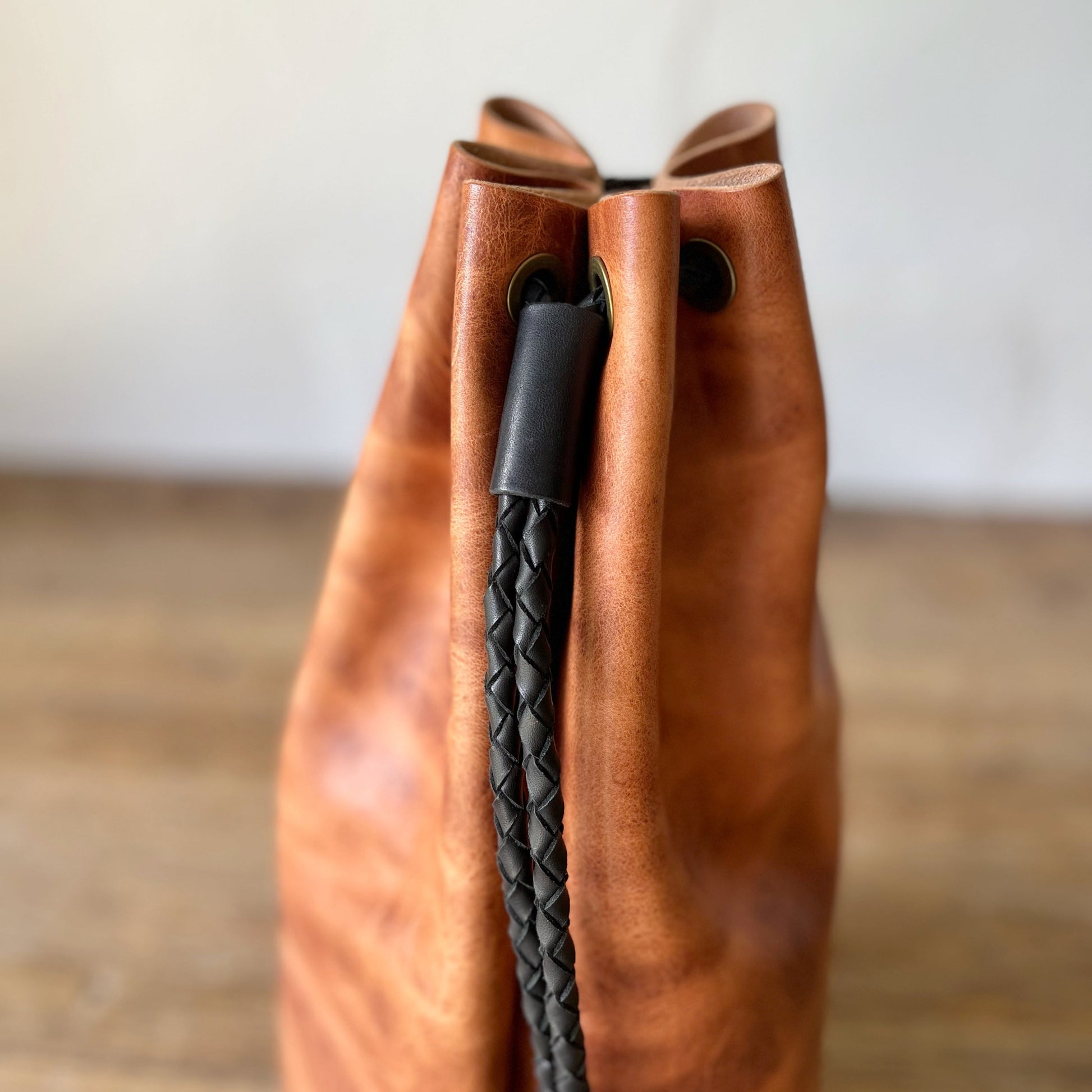 Brown leather bag with a black braided handle on a wooden surface.