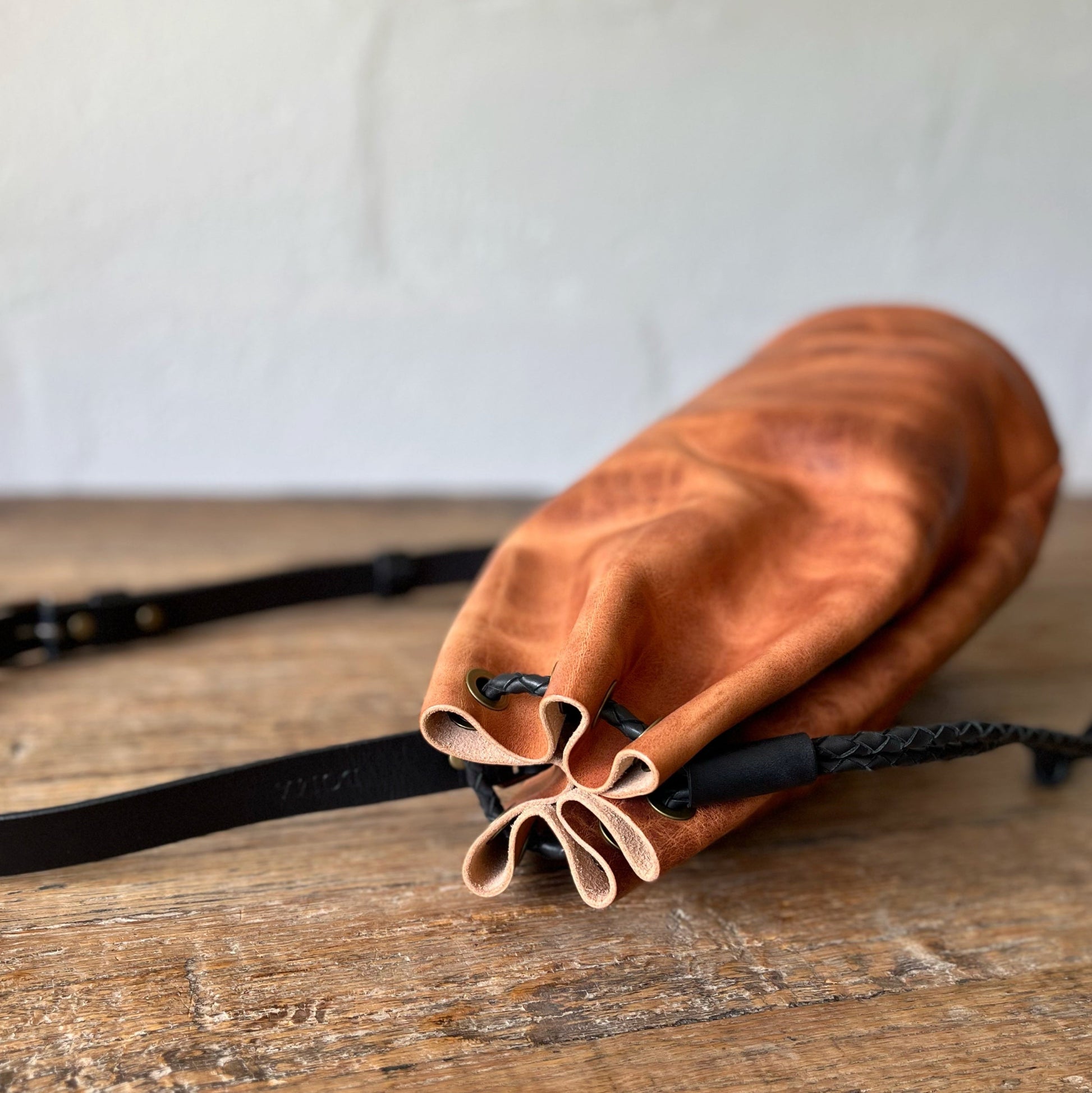Brown leather drawstring bag on a wooden surface with a white background
