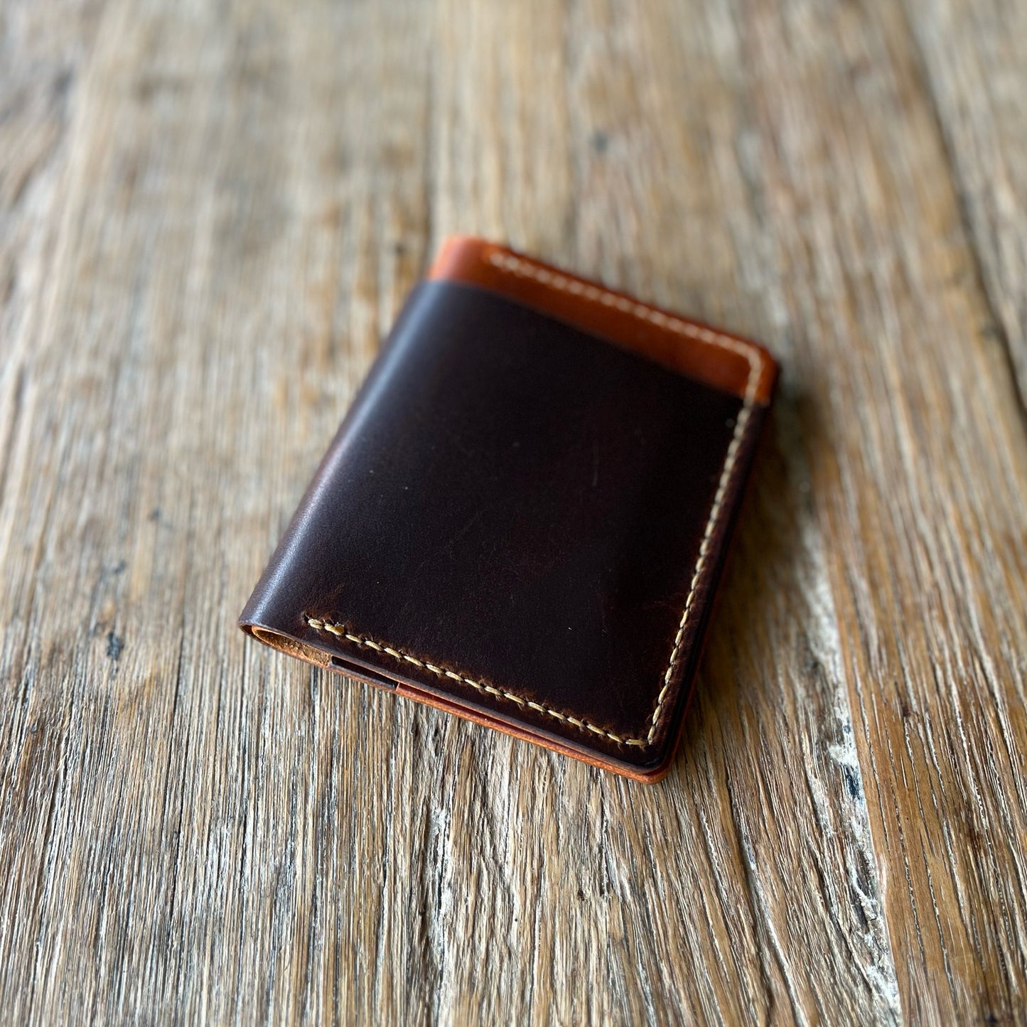 A two-toned, brown and black bifold cash wallet made of leather, placed on a wooden surface.