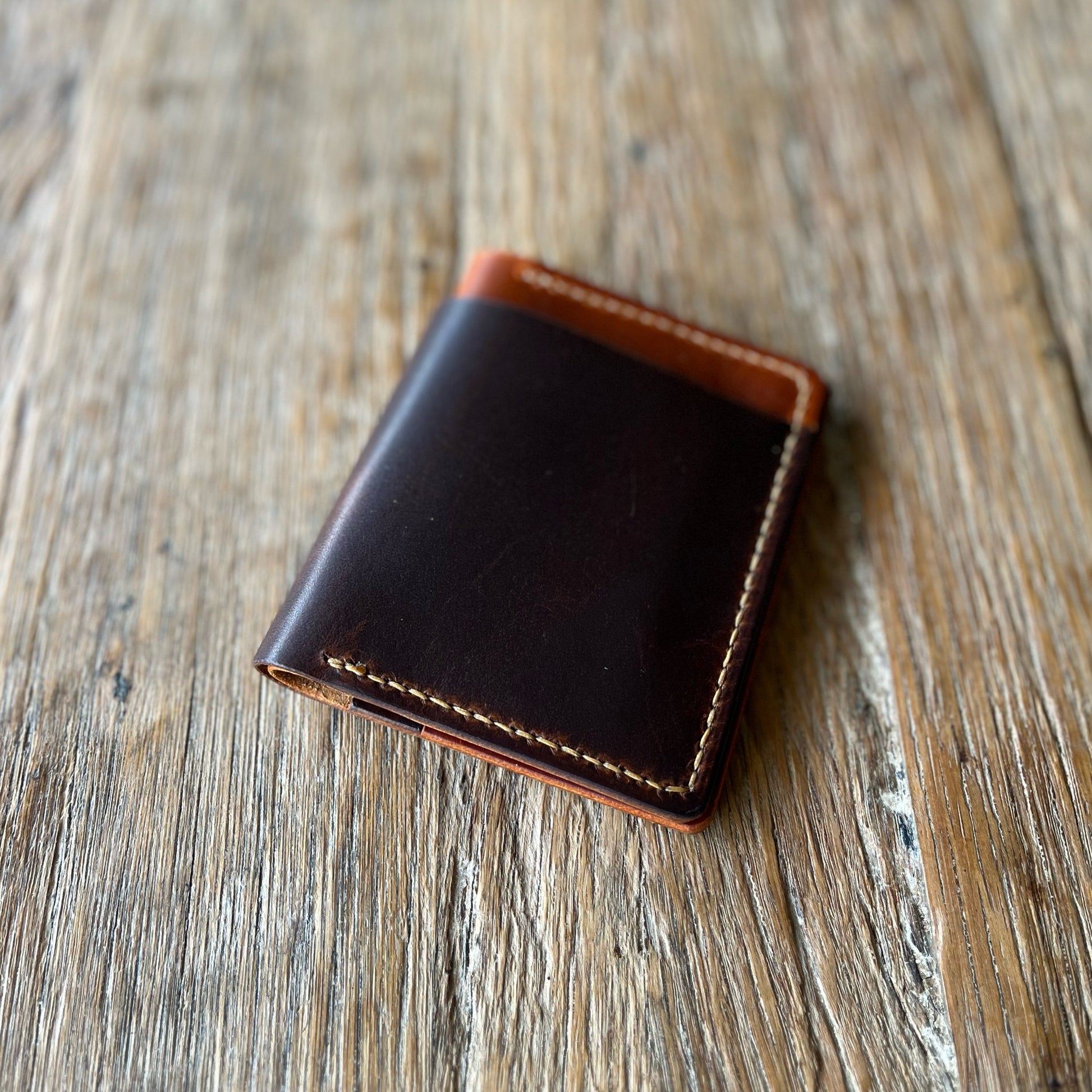 A two-toned, brown and black bifold cash wallet made of leather, placed on a wooden surface.