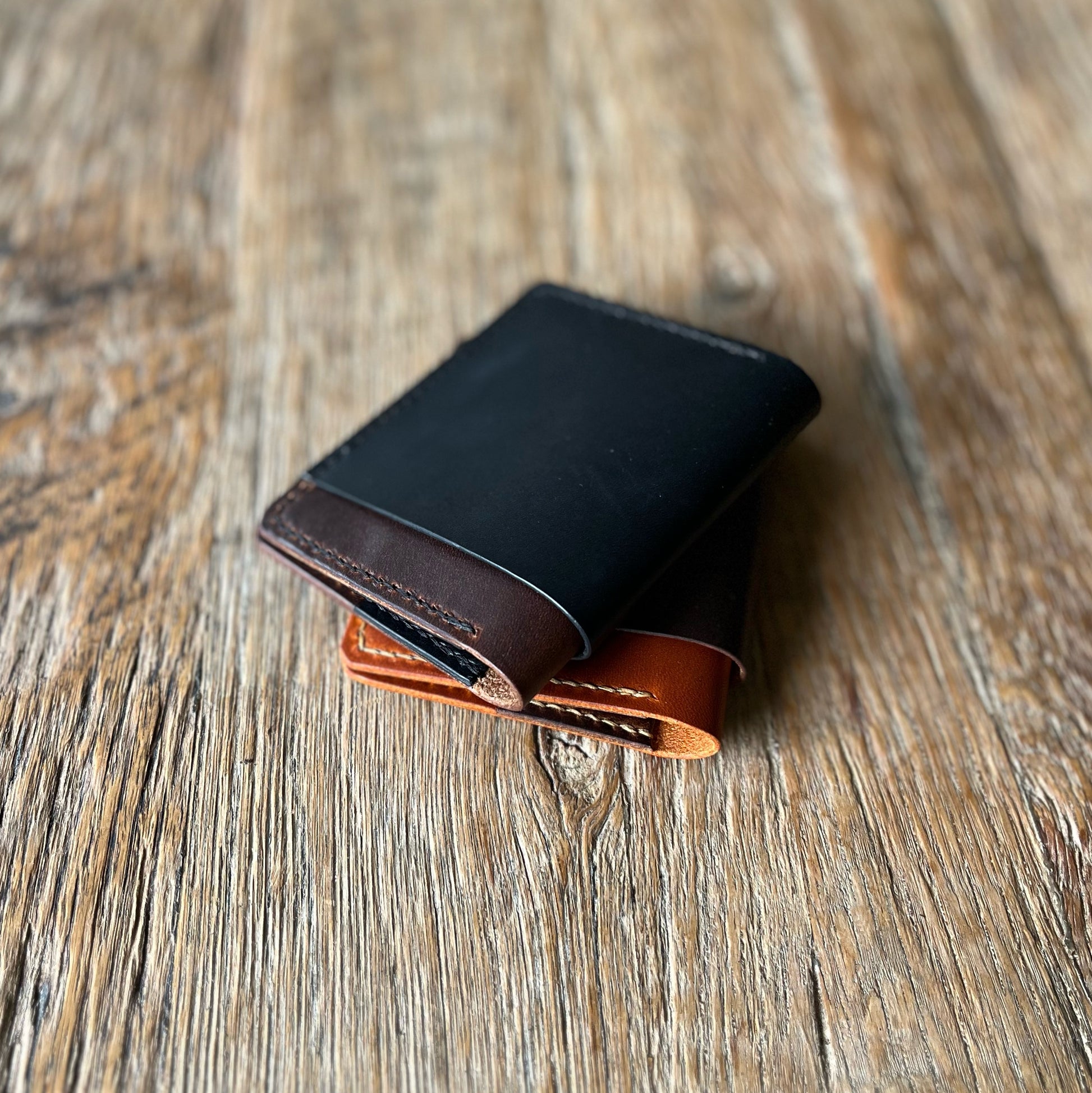 A two-toned, brown and black bifold cash wallet made of leather, placed on a wooden surface.