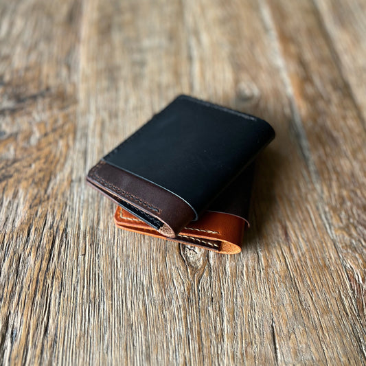 A two-toned, brown and black bifold cash wallet made of leather, placed on a wooden surface.